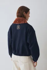 Campera bomber de paño color azul marino, con cuello de piel sintética en color marrón desmontable, cierre frontal y puños elásticos. Presenta logo bordado en el frente y bolsillos laterales.