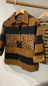 Camisa de tejido de punto a rayas horizontales en color marrón y negro, con cuello camisero, cierre frontal de botones y bolsillos frontales de cuero con estampado animal print.