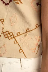 Chaleco de algodón color beige con estampado geométrico en tonos bordó y marrón. Presenta escote en V, cierre frontal con botones y corte recto.
