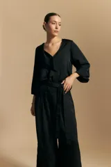 Blusa negra de satén con escote en V y detalle de volados frontales. Presenta mangas largas con puños abotonados y una silueta fluida.