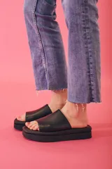 Sandalias tipo chinelas con plataforma plana y tira ancha de cuero negro sobre el empeine.