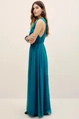Vestido largo color verde turquesa, confeccionado en gasa con forrería a tono. Posee escote en V profundo con volados, sin mangas, y corte en la cintura con lazo ajustable.