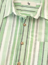 Camisa de manga corta a rayas verticales azules y blancas, con cuello clásico, corte cuadrado y calce relajado. Presenta botones de coco con logo y parche distintivo de Polonio. Confeccionada en Italia con mezcla de lino y algodón.