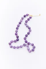 Collar de esferas de piedra amatista en tonos violeta, ensartadas con hilo a tono y con cierre metálico dorado con cadena de alargue.