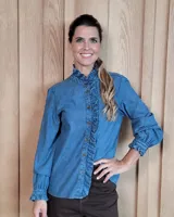 Camisa de jean con volados en el frente y cuello alto. Presenta mangas largas con puños elásticos y detalle de volados en los mismos, cierre frontal con botones.