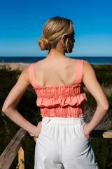 Crop top color salmón, fruncido con elásticos y tirantes finos. Detalles de volados en los bordes superior e inferior.
