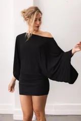 Blusa fluida de color marrón, con diseño holgado, escote bote que deja un hombro al descubierto y mangas anchas y cortas.