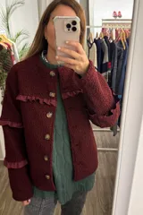 Campera de tela bouclé color bordó, con diseño de cuello redondo y cierre frontal mediante botones. Presenta detalles de volados en tela agamuzada en el pecho y en las mangas.