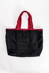 Bolsa de compras tipo tote, de color negro con detalles y asas en color rojo. Diseño plegable y ligero.