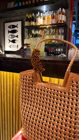 Bolso tipo tote bag de cuero trenzado a mano, en tonos marrón y negro, con asas trenzadas.