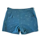 Short de baño color azul petróleo con estampado sutil de palmeras. Presenta una pretina fija con hebillas metálicas laterales para ajuste, cierre frontal con botón a presión, dos bolsillos laterales y un bolsillo trasero. Incluye interior con mesh hipoalergénico.
