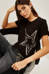 Remera negra de viscosa con cuello redondo y manga corta, presenta una estampa central de estrella grande decorada con lentejuelas brillantes.
