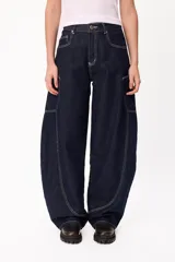 Jean de corte amplio y tiro medio, confeccionado en denim azul oscuro con costuras a contratono en color blanco. Presenta un diseño de pierna curva con bolsillos laterales integrados.