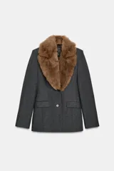 Blazer entallada de color gris oscuro, confeccionada en tejido con algodón. Presenta un cuello solapa con aplicación de pelo sintético desmontable, manga larga, bolsillos delanteros con solapa y cierre frontal con botones.