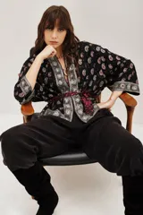 Kimono corto de estilo bohemio, confeccionado en viscosa negra con estampado paisley y detalles bordados en los bordes frontales y mangas. Presenta mangas tres cuartos y un lazo ajustable en la cintura con estampado animal print.