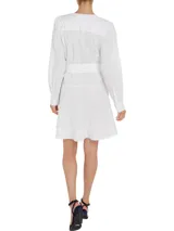 Vestido camisero corto color blanco, confeccionado en algodón orgánico. Presenta cuello en V, cierre frontal con botones, mangas largas abullonadas, cinturón de lazo ajustable en la cintura, bolsillos laterales y detalle de encaje calado en forma de escalera.