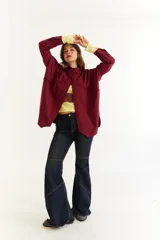 Camisa de corte oversize color bordó, con cuello clásico, cierre frontal de botones y detalle de trenzado horizontal en la parte superior delantera. Posee mangas largas con puños abotonados.