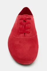 Zapatilla deportiva estilo blucher de piel color rojo, con pespuntes en el cuerpo, cierre mediante cordones y punta redonda.