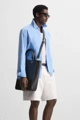 Bolso tipo shopper color negro, con compartimento principal con cierre mediante imán, bolsillo interior con cierre, detalle de arnés en la parte delantera, dos asas de mano y asa de hombro ajustable y extraíble.