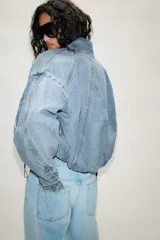 Cazadora bomber de denim con cuello subido, manga larga y cierre frontal con cremallera y botones a presión ocultos. Presenta costuras verticales decorativas y bajo con ajuste elástico.