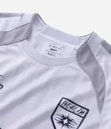 Remera de manga larga estilo deportivo con corte boxy, confeccionada en poliéster. Presenta cuello redondo, paneles laterales en tejido texturizado y estampados gráficos estilo tribal y lettering gótico en el frente.