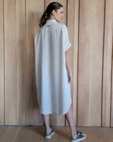 Túnica midi de lino con corte holgado, cuello camisero y cierre frontal completo con botones. Presenta mangas cortas con dobladillo y bolsillos laterales amplios.