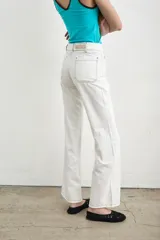Jeans de denim blanco de tiro alto, corte recto y amplios bolsillos frontales aplicados. Cuenta con cierre frontal abotonado con múltiples botones metálicos a la vista y pespuntes en contraste.