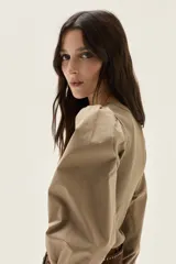 Top de calce ajustado color marrón, con escote cuadrado y mangas largas abullonadas de tela lisa. Los puños de las mangas son elastizados.