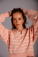 Buzo de punto color salmón con rayas horizontales blancas, cuello alto con cierre frontal y mangas largas abullonadas.