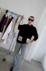 Campera tejida con textura vanizada a rayas horizontales en blanco y negro, con cierre frontal y flecos negros en forma de V en el pecho.