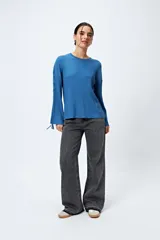 Sweater color crema de tejido de canalé con detalle de trenzado en las mangas y terminación con lazo ajustable.