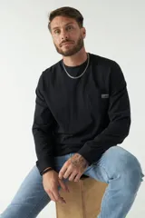 Remera de hombre negra de manga larga con puños, escote redondo y bolsillo en el pecho con etiqueta de marca.