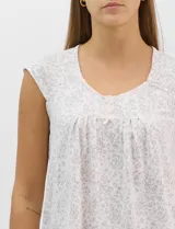 Pijama compuesto por remera sin mangas con escote redondo, botones frontales y detalle de puntilla, acompañado de un pantalón capri con cintura elástica. Presenta un estampado floral en tonos rosados sobre base gris.