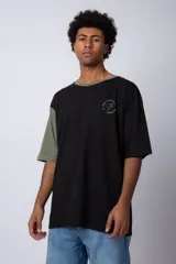 Remera de corte oversize en color beige, con cuello redondo en contraste negro y una manga en color negro. Presenta un pequeño estampado circular en el pecho con la frase 'Don't worry, be happy'.