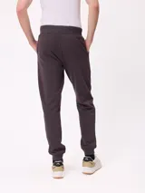 Babucha jogger color gris oscuro, con cintura elástica ajustable con cordón, bolsillos laterales y puños elásticos en los tobillos. Presenta un logo estampado en el muslo izquierdo.