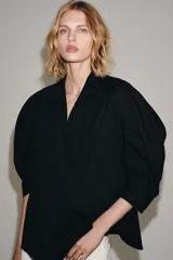Camisa de cuello redondo y manga corta abullonada, color negro, de corte recto con aberturas laterales y cierre frontal con botones. Perteneciente a la colección ZARA Woman Collection.