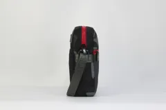 Morral bandolera negro con estampado camuflado en tonos grises en la parte superior y logo de los Chicago Bulls bordado en rojo y blanco en la parte inferior. Tiene doble cierre rojo, correa regulable y logo de la NBA en el lateral.