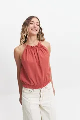 Blusa sin mangas color terracota, con cuello halter fruncido y elástico en la cintura. Presenta un diseño holgado y fresco con acabado tipo lino.