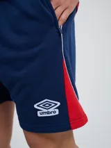Bermuda deportiva Umbro del Club Nacional de Football, modelo Nexo para hombre, en color azul marino con detalles en rojo y blanco. Cuenta con el escudo del club bordado en la pierna derecha y el logo de Umbro en la izquierda, además de cordón ajustable en la cintura.