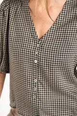 Blusa de algodón con estampado de cuadros vichy en tonos negro y blanco. Presenta escote en V, cierre frontal con botones y mangas cortas abullonadas con terminación elástica.