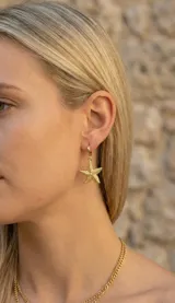 Aros tipo argolla pequeña de acero dorado con dije colgante en forma de estrella de mar con textura punteada.