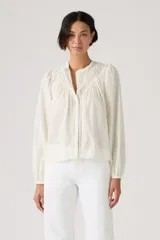 Blusa color crudo de manga larga, con cuello mao y detalles de encaje y bordados en el frente. Presenta diseño abotonado oculto y mangas abullonadas con puños elásticos.