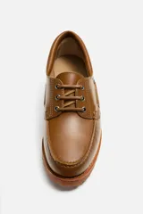 Zapato tipo náutico de cuero color marrón, con cordones, ojales metálicos laterales y suela de goma con volumen y relieve dentado.