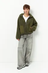 Buzo negro de teddy con cuello alto y cierre de cremallera parcial. Presenta bolsillos de nylon en la parte inferior delantera.