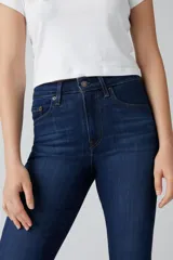 Jean de corte flare con tiro alto, confeccionado en denim azul oscuro con efecto desgastado. Presenta cierre de cremallera con botón metálico, cinco bolsillos tradicionales y costuras reforzadas.