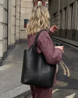 Cartera tipo tote bag de eco cuero negro, con diseño de paneles pespunteados y doble asa larga para hombro.