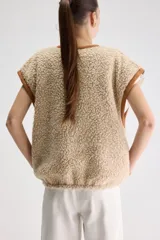 Chaleco reversible oversize de tejido tipo corderito, color beige con detalles de costuras y ribetes en marrón y cierre frontal con cremallera.