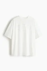 Remera deportiva de punto de algodón color blanco, de corte oversized con mangas cortas, hombros caídos y cuello redondo ribeteado. Presenta un estampado frontal en relieve dentro de un óvalo.