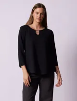 Blusa negra en tejido labrado con cuello redondo, escote en V y aplique metálico. Manga tres cuartos.