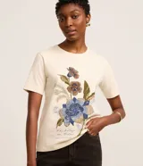 Remera de algodón color beige con cuello redondo y mangas cortas. Presenta un estampado frontal con diseño floral de estilo mosaico y texto en la parte inferior.